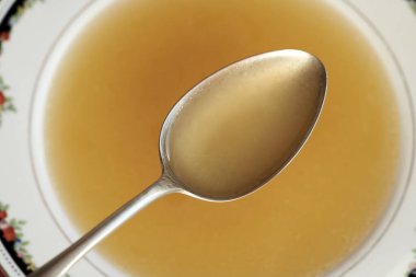 Çorba kasesinin üstündeki metal kaşıkta kemik suyu çorbası.