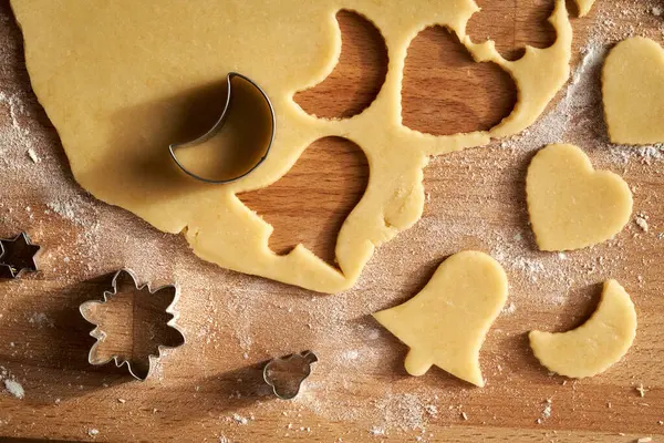 Cutting out bell, moon and heart shapes from rolled out dough to prepare Linzer Christmas cookies