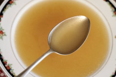 Tabağın üstündeki metal kaşıkta tavuk çorbası.