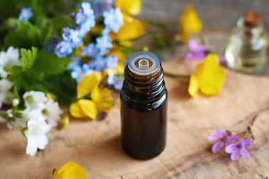 Masasında renkli çiçekler olan koyu renkli bir aromaterapi şişesi.