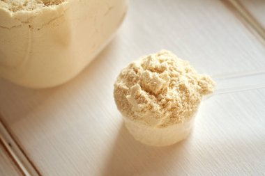 Bir kepçedeki beyaz protein tozu ve beyaz bir masada bir kavanozda