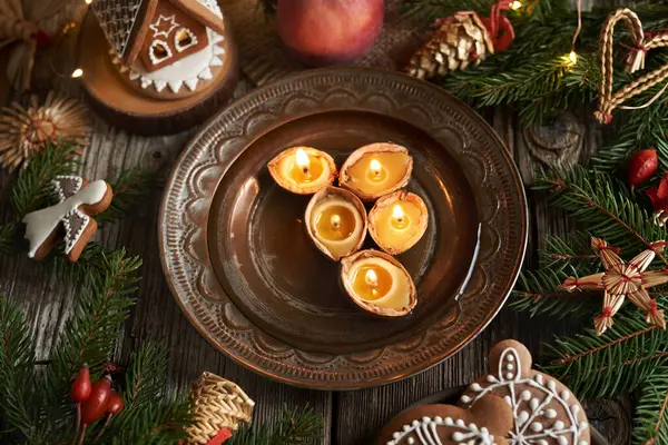 Christmas candles made of bees wax floating in a bowl of water, with apples and gingerbread house