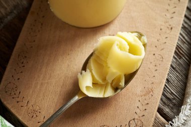 Ahşap bir masada metal kaşık üzerinde açık bir tereyağı.