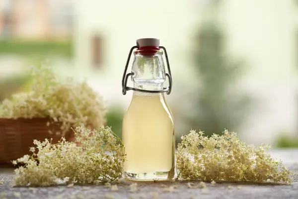 A bottle of homemade elderberry flower syrup on a table outdoors