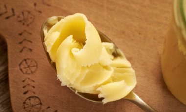 Ahşap bir masada metal kaşık üzerinde açık bir tereyağı.