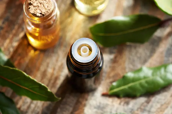 stock image A dark bottle of aromatherapy essential oil with fresh bay leaf on a wooden table, top view