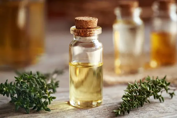 A transparent bottle of aromatherapy essential oil with fresh thyme twigs on a table