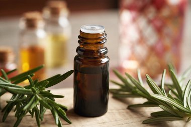 Ahşap bir masada taze biberiyeli koyu bir aromaterapi şişesi.