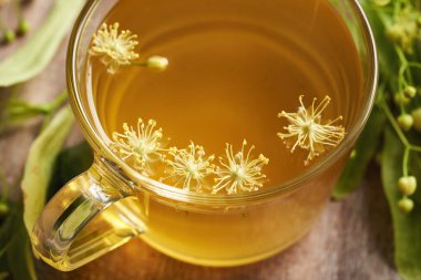 Linden ya da Tilia çiçekleri bir fincan bitkisel çayın içinde, masanın üzerinde, kapat.