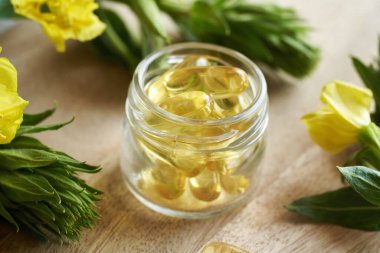 İçinde çiçek açan Oenothera biennis bitkisiyle birlikte akşam çuha çiçeği yağının kapsülleri olan cam bir şişe. Besleyici takviye.