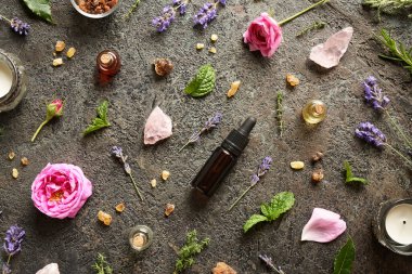 Tütsülenmiş aromaterapi şişeleri, lavanta çiçekleri, lavanta çiçekleri ve koyu arkaplanda gül kuvars taşları.