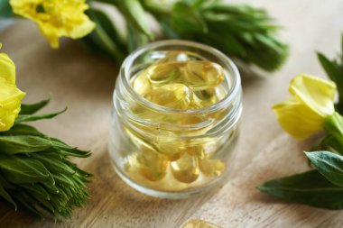 Çiçek açan Oenothera biennis bitkisiyle birlikte bir kavanoz jel kapsülü. Sağlıklı besin desteği.