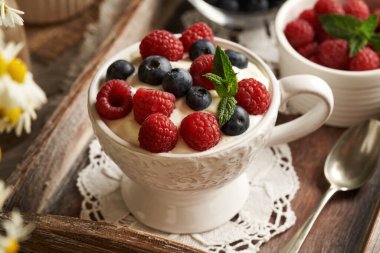 Bir kasede keten tohumu yağıyla harmanlanmış süzme peynir, masada taze ahududu ve yaban mersini.