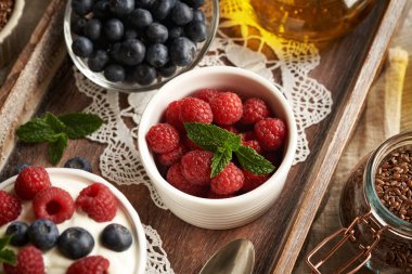 Raspberries in a bowl, with blueberries, cottage cheese and flax seed oil in the background clipart