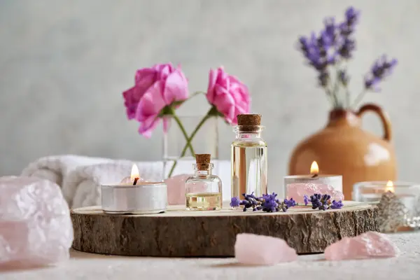 stock image Bottles of aromatherapy essential oil with fresh lavender and rose de Mai flowers, rose quartz stones and spa towels on white background