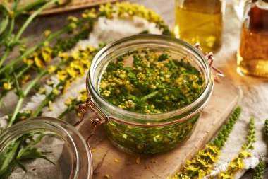 Ev yapımı bitkisel tentürü hazırlamak için içi doğranmış taze tarımsal çiçeklerle dolu cam kavanoz.