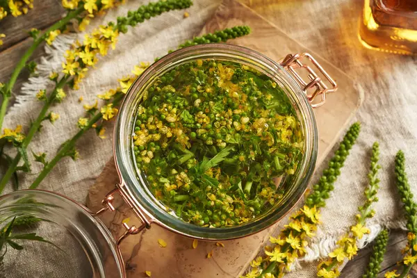 stock image Preparation of herbal tincture with fresh blooming agrimony - macerating the plant in alcohol, top view