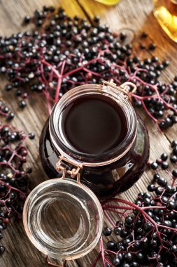 Arka planda taze elder çilekleri olan cam bir kavanozda ev yapımı siyah yaşlı şurubu.
