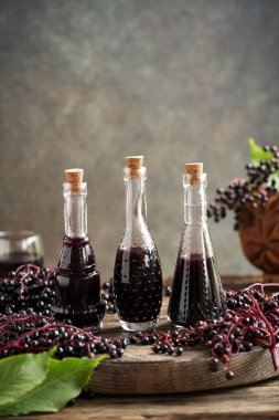 Üç şişe ev yapımı siyah yaşlı şurubu. Üzerinde taze mürver şerbeti var.