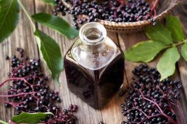 Bir şişe ev yapımı siyah yaşlı şurubu ve ahşap bir masada taze mürver.