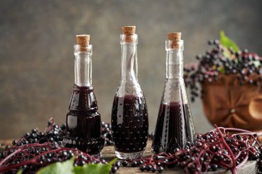 Üç şişe ev yapımı siyah yaşlı şurubu ve masada taze elderberry.