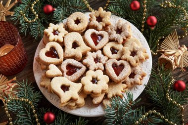 Bir tabak Linzer Noel kurabiyesi çilek reçeli ve şekerle doldurulmuş ladin ağacı dalları ve saman süslemeleri.