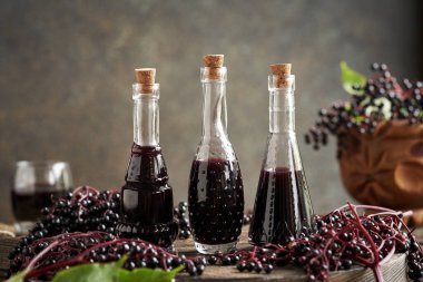 Üç şişede siyah yaşlı şurubu ve masada taze mürver.