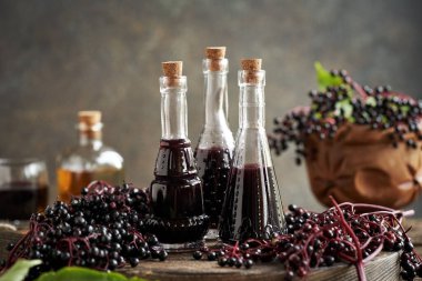 Üç şişede siyah yaşlı şurubu ve bir masada taze elderberry.