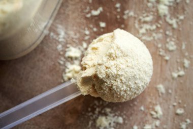 Masadaki bir kaşık içindeki beyaz protein tozu. Fitness için besin takviyesi.