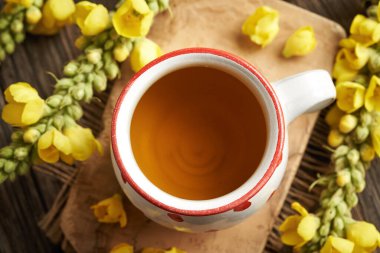Üzerinde taze Verbascum çiçekleri olan beyaz noktalı bir bardak Mullein çayı.
