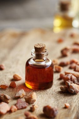 A bottle of styrax essential oil with styrax benzoin resin on a wooden table clipart