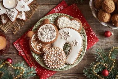 Yeşil bir tabakta beyaz kremayla süslenmiş ev yapımı zencefilli Noel kurabiyeleri ladin ağacı dalları, cevizler ve mumlar.