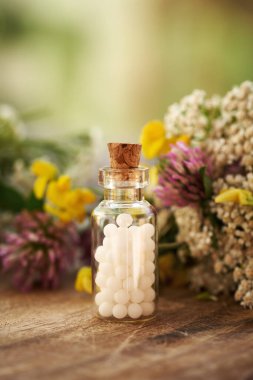 Bir şişe beyaz homeopatik hap ya da yazın renkli taze çiçekler ve otlarla dolu küreler.