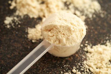 Koyu arkaplanda bir kaşık içindeki beyaz protein tozu