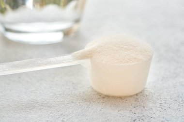 Plastik bir kaşık içindeki kolajen tozu ve parlak arka planda bir bardak su.