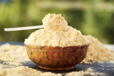 Bir kasede beyaz protein tozu ve dışarıda ölçü kabı, yeşil bokeh