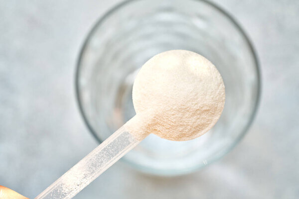 Collagen powder in a plastic measuring spoon above a glass of water, top view