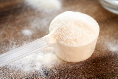 Tahta bir masada plastik bir kepçenin içindeki kolajen tozunun yakınına.