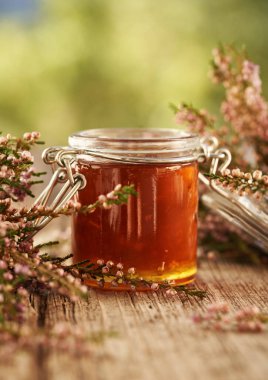 Herbal syrup in a glass jar with fresh wild heather flowers from the forest, outdoors with copy space clipart