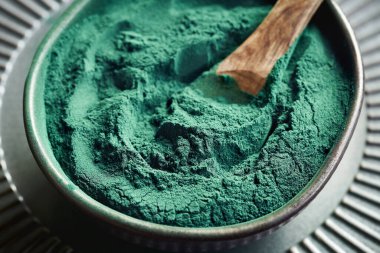 Kasedeki tahta kaşıkta yeşil spirulina yosun tozu. Besleyici takviye