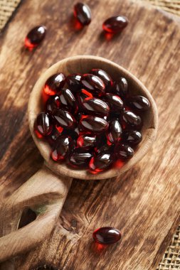 Masadaki tahta kaşıkta kırmızı kril yağı hapları ya da küreler.