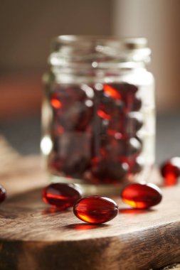 Red krill oil pills or globules on a wooden table and in a glass jar clipart