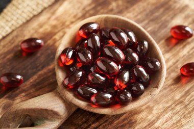 Red krill oil pills or globules on a wooden spoon, closeup clipart