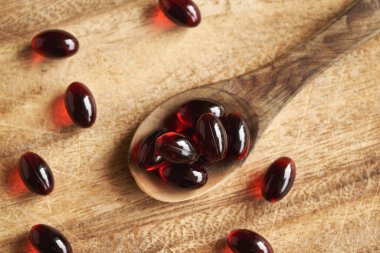 Red krill oil pills or globules on a wooden spoon on a table, top view clipart