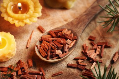 Tahta kaşıkta kırmızı sandal ağacı parçaları, balmumu mumları ve çam ağacı dalları.