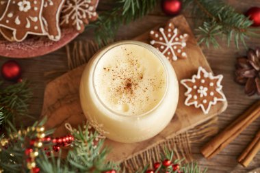 Bir bardak ev yapımı yumurta likörü, zencefilli kurabiye ve Noel süsü.