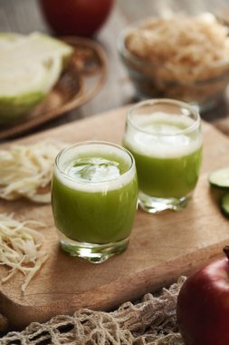 İki fincan taze yeşil lahana ve ahşap masada kırmızı elmalı salatalık suyu.