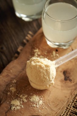 Beyaz protein tozu bir kepçede taze doğal sütle ahşap bir masada.