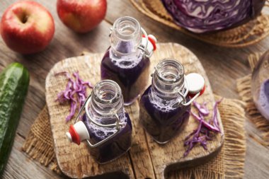 Masada taze elma ve salatalık ile üç şişe mor lahana suyu.