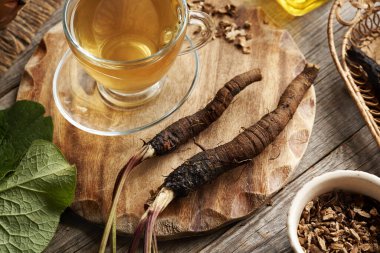 Tahta bir masada taze burdock kökünden yapılmış bir fincan bitki çayı.
